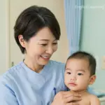 A smiling healthcare professional in blue scrubs holding an infant, demonstrating the concept of taking care of a patient.