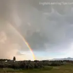 A vibrant rainbow arching across a dark, stormy sky over a rural landscape
